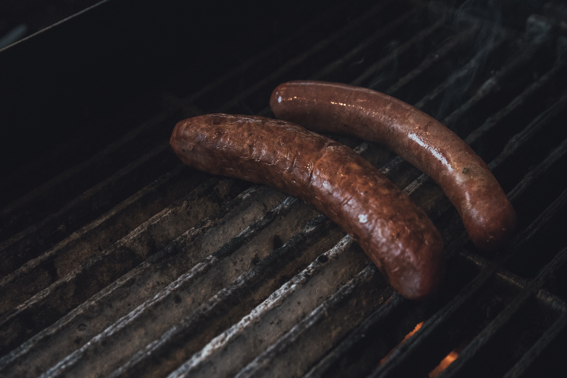 Two sausages cooking on the grill with fire glowing underneath