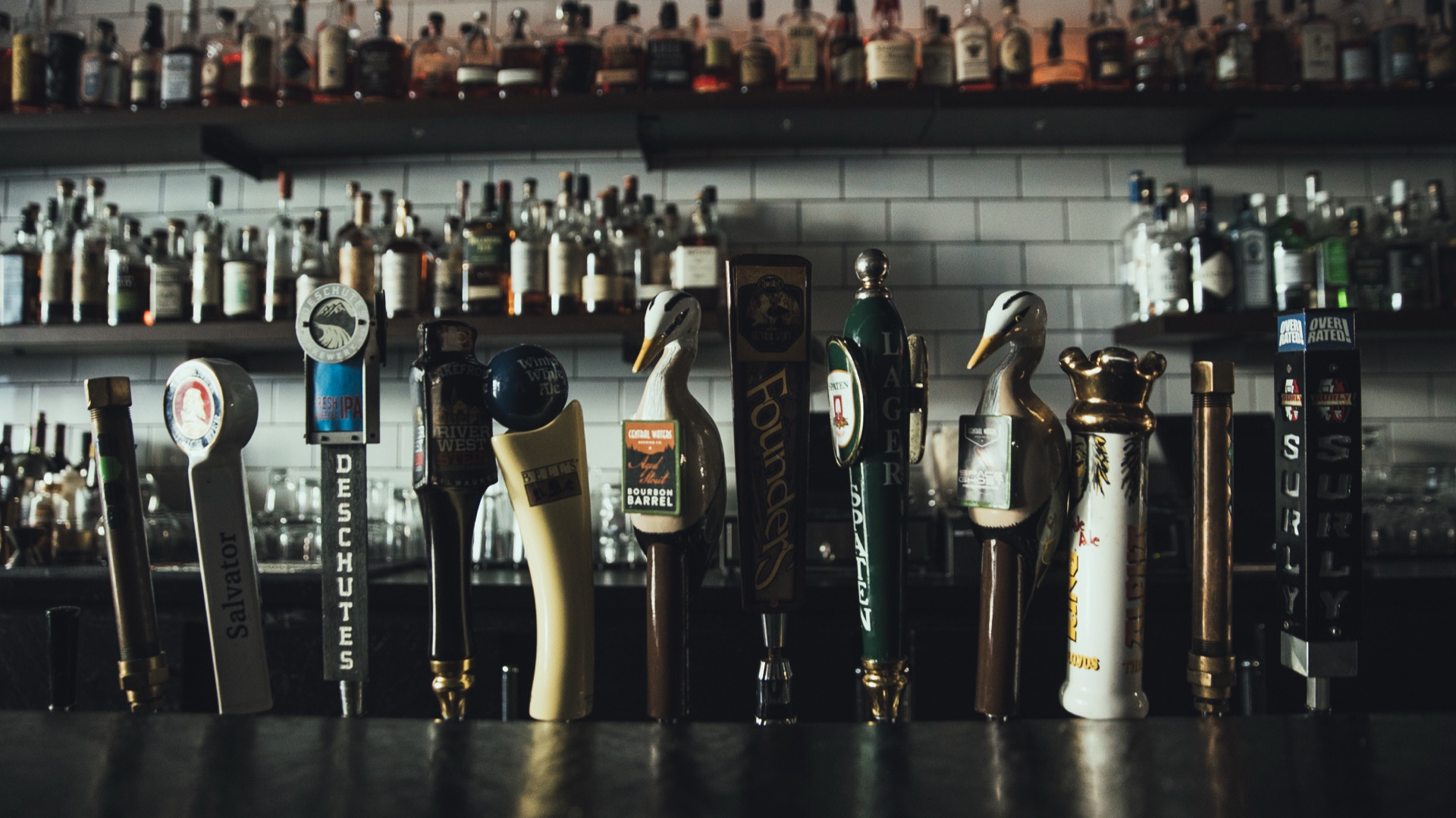 Craft beer tap handles lined up along the bar with bourbon bottles behind
