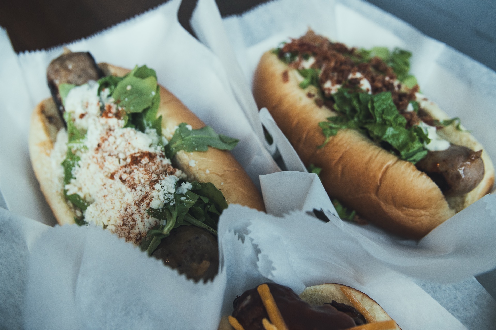 Two gourmet sausages in buns with creative toppings viewed from above