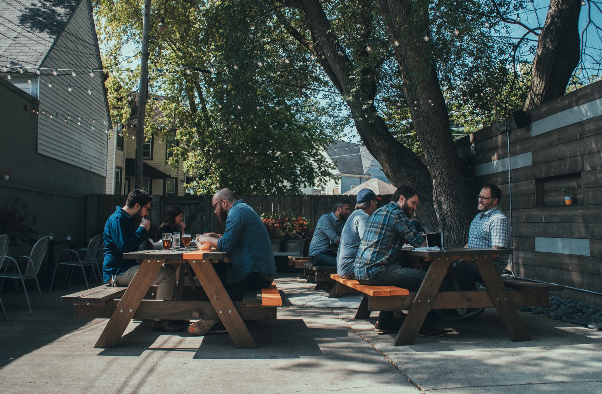 Outdoor patio with picnic tables, string lights, and people eating under the trees
