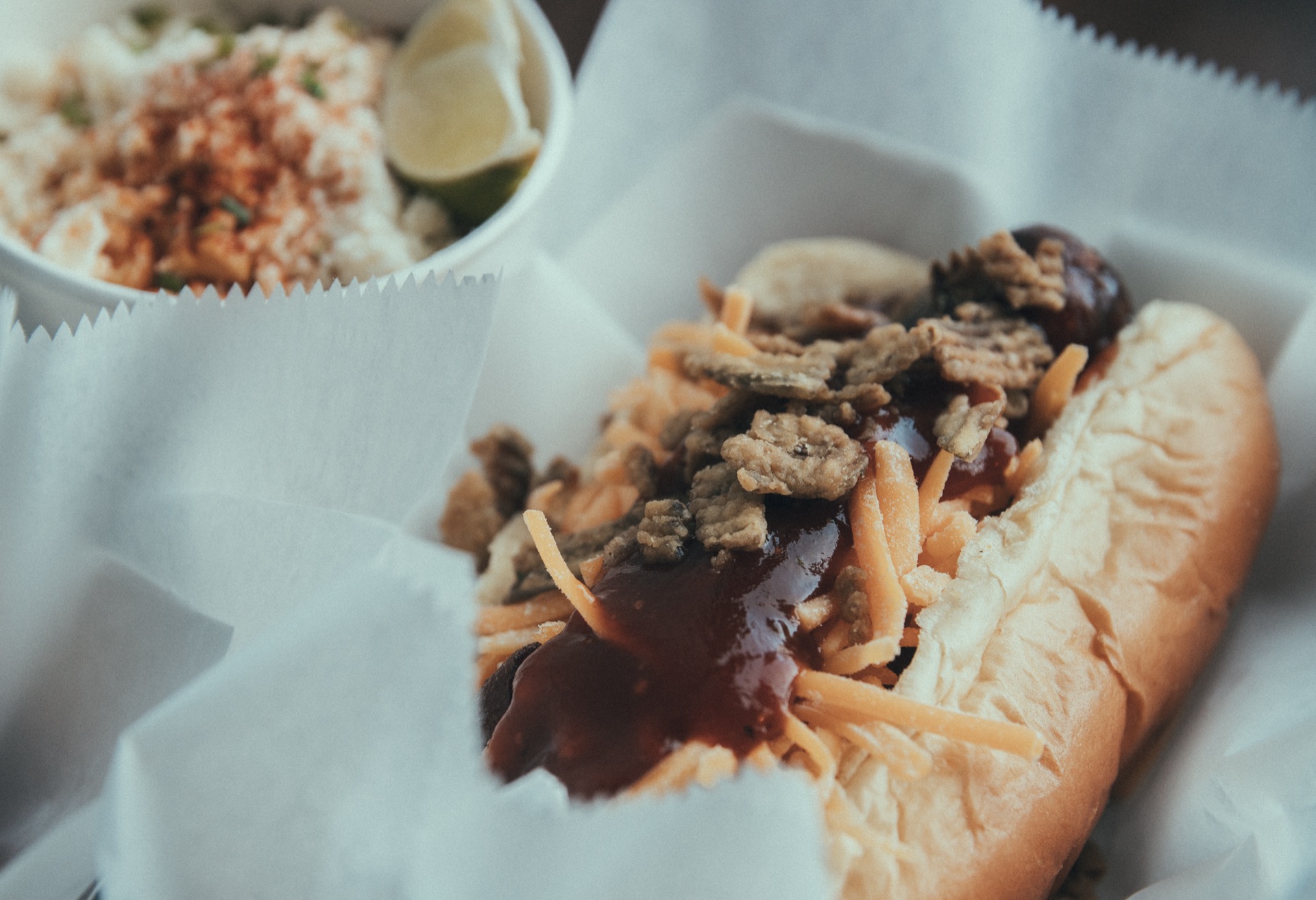 Loaded sausage in a bun topped with BBQ sauce, cheese, and fried onions