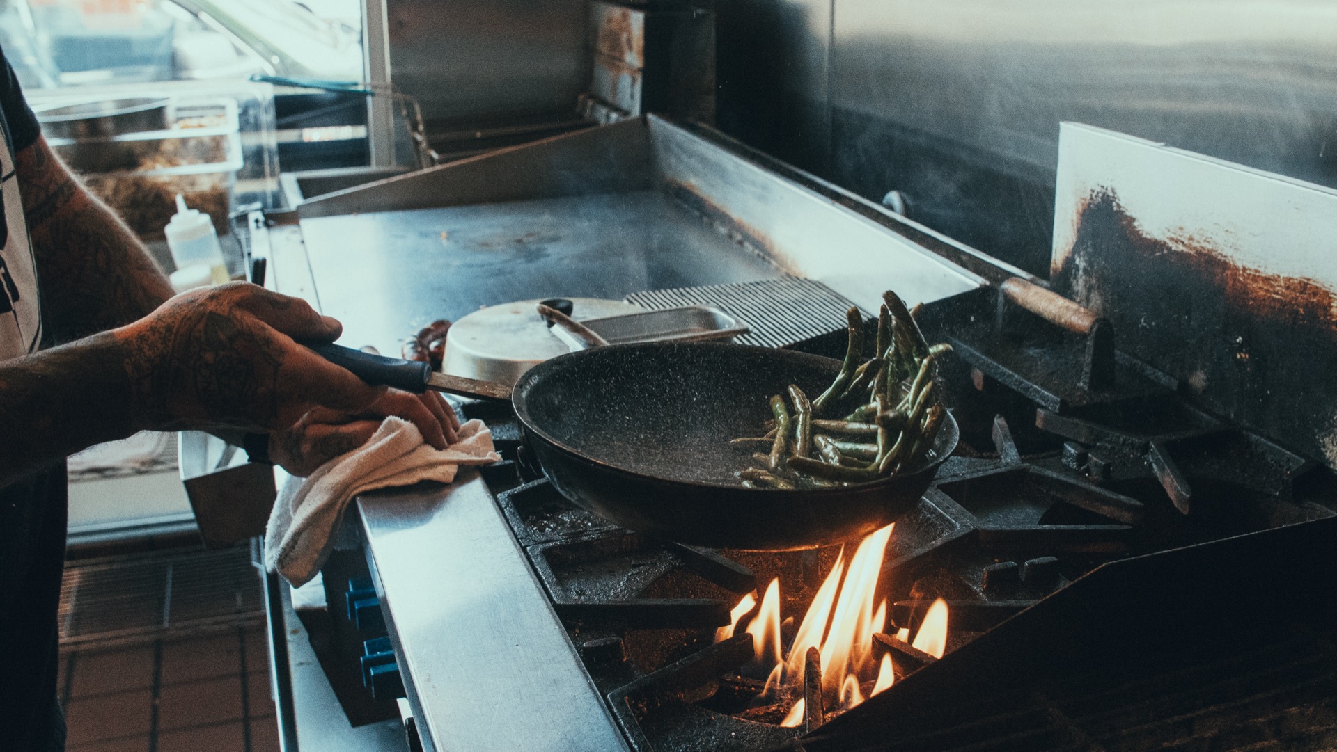 Cook's hands gripping a skillet over open flames in the kitchen