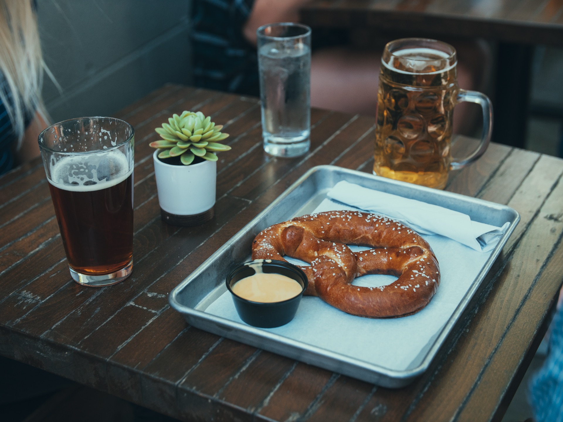 Soft pretzel with cheese sauce surrounded by glasses of craft beer