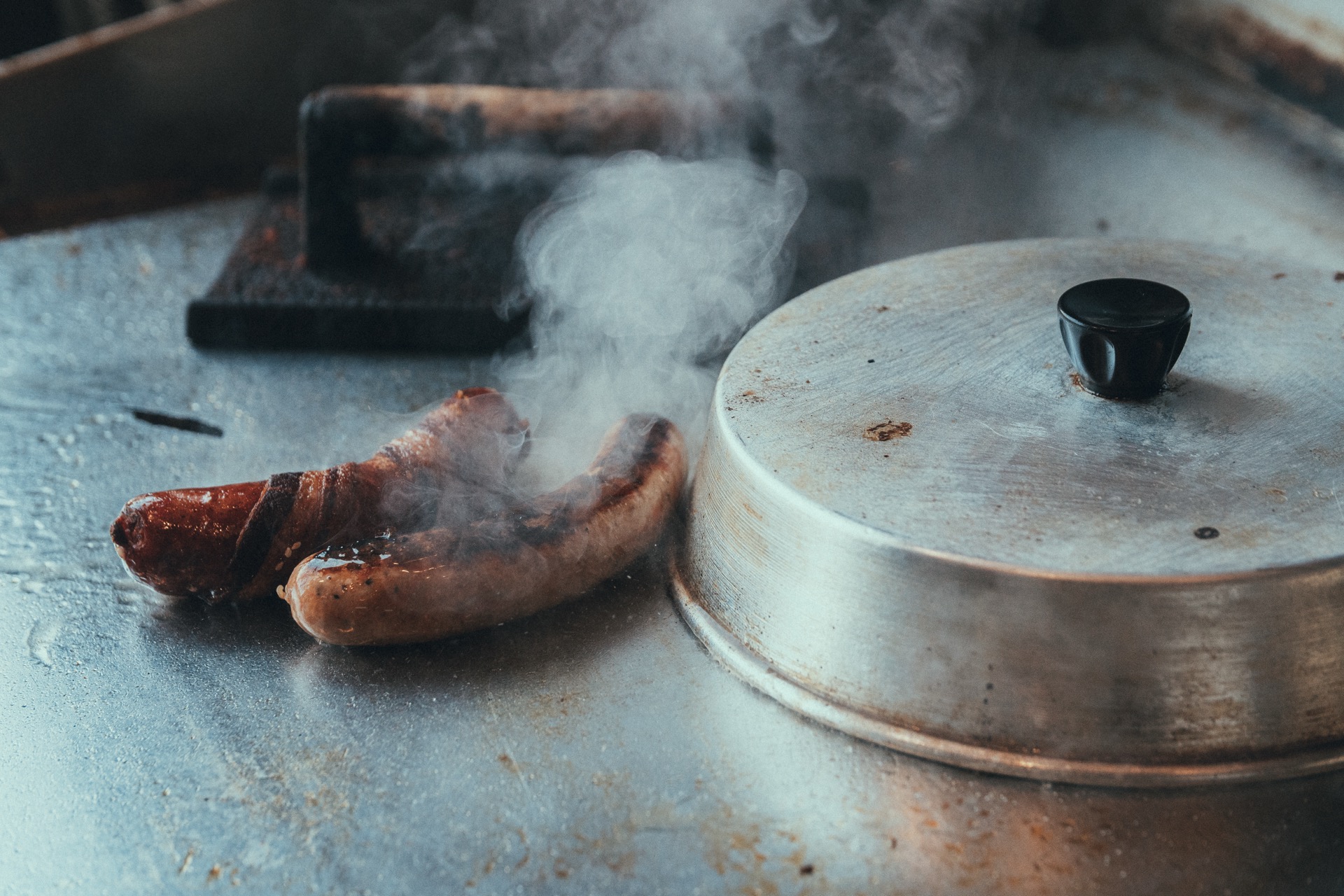Sausages cooking on the flat-top griddle with steam rising